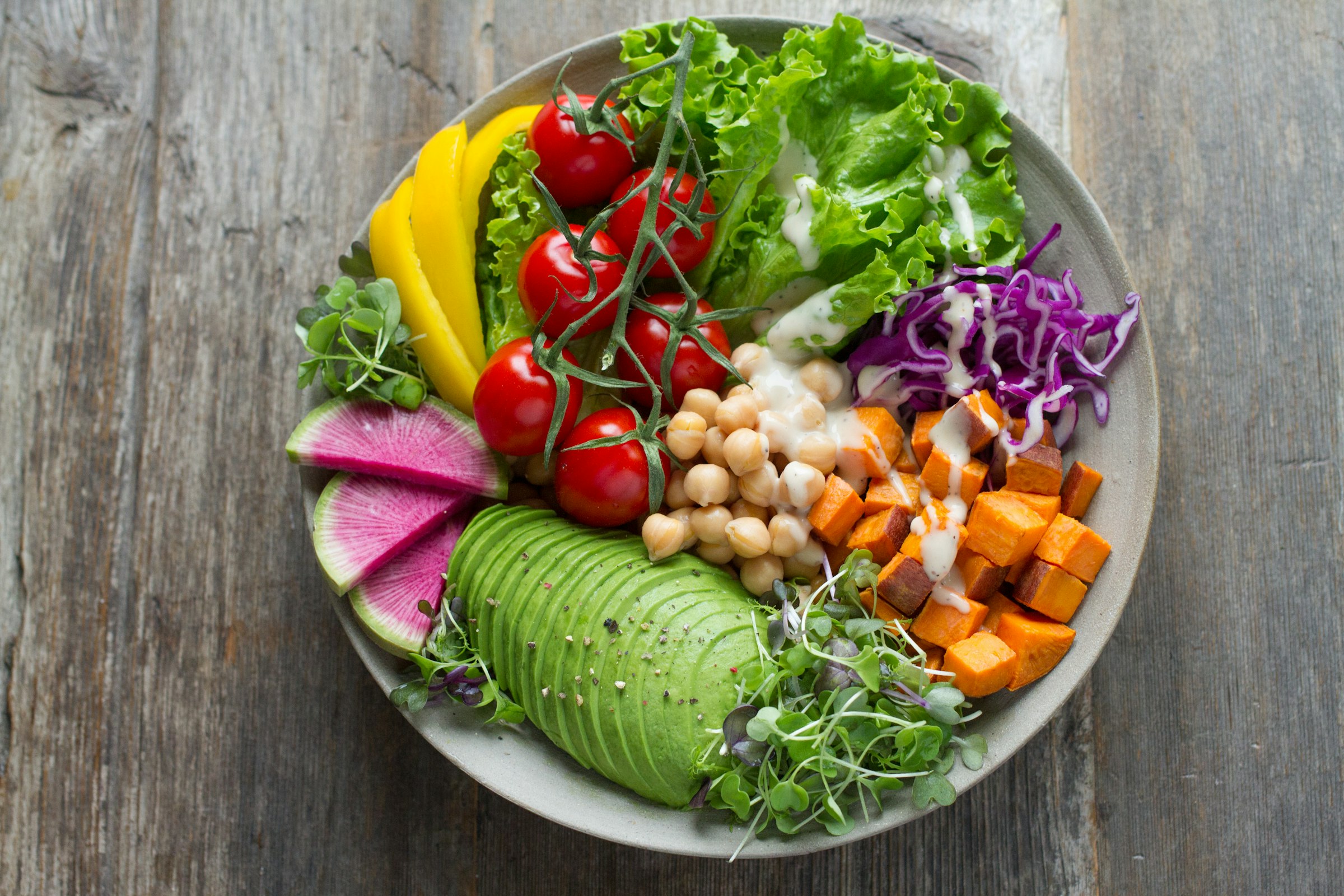 Colourful wholefood bowl with avocado, tomatoes, chickpeas and fresh greens on a wooden surface