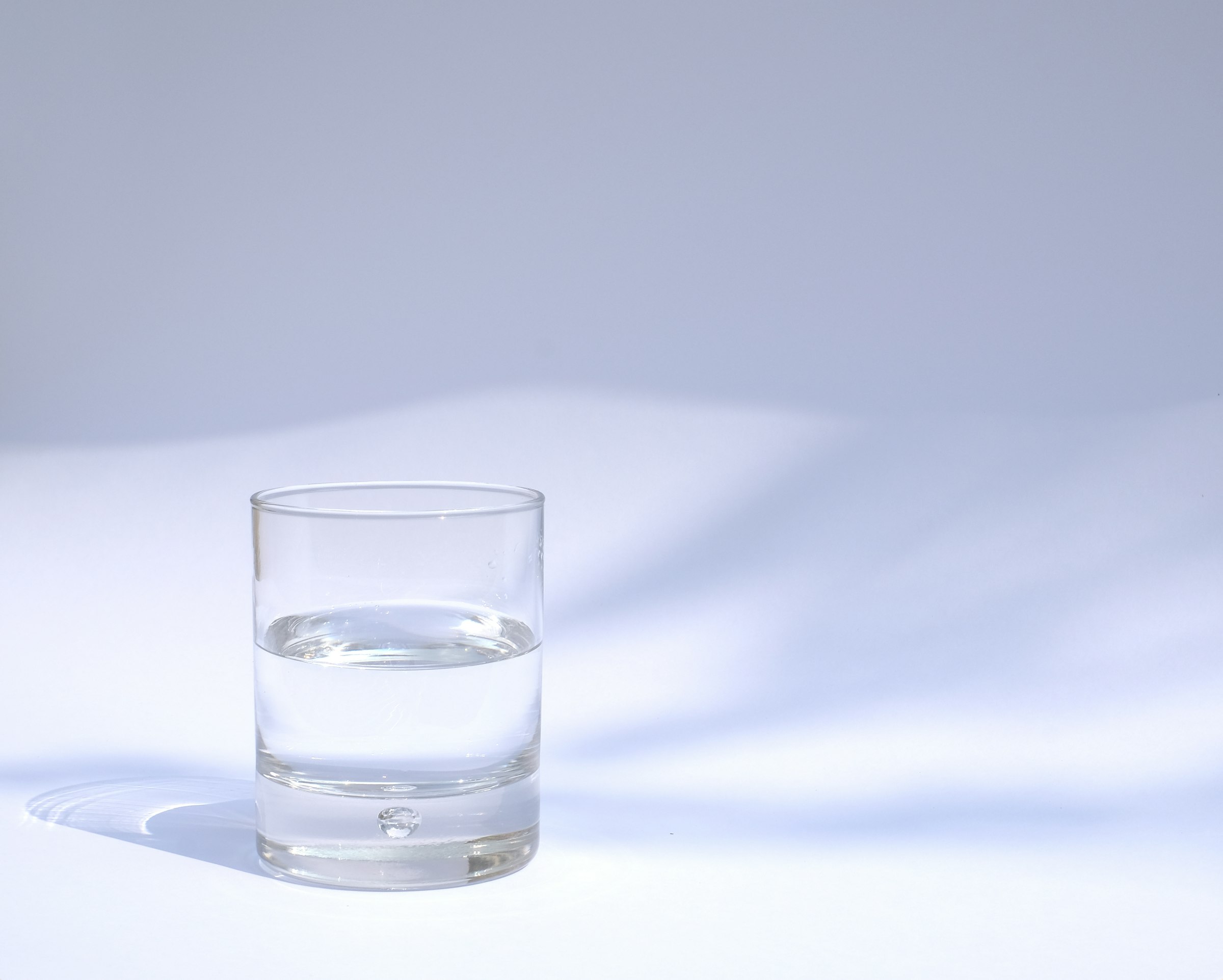 A clear glass of water casting soft shadows against a pale blue background