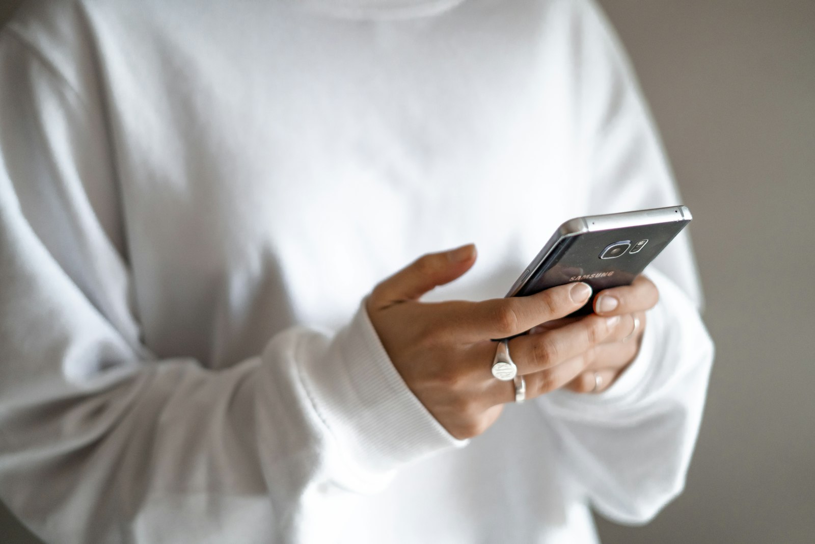 Person in a white sweatshirt holding a smartphone against a neutral background
